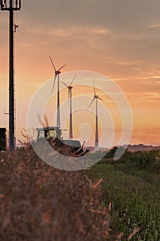 Beautiful shot of a tractor working in the fields of wheat with wind power plants in the background