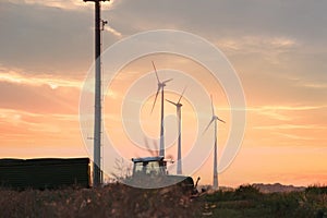 Beautiful shot of a tractor working in the fields with wind power plants in the background