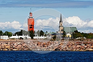 Beautiful shot of water near a shore with a red clock tower and a cloudy sky in the background