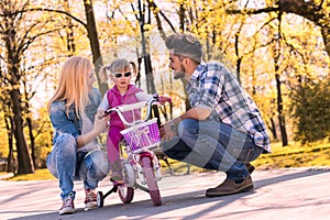 Beautiful shot of young Caucasian parents teaching their daughter how to ride a bike