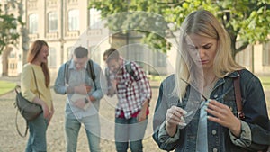 Beautiful shy blond girl smiling at camera as people laughing at her at the background. Confident intelligent Caucasian