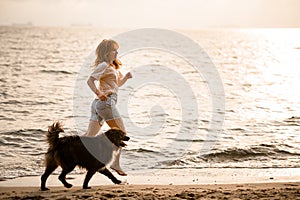 beautiful side view on woman running along sandy beach at water with her dog