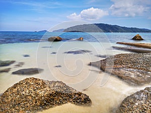 The beautiful silky smooth water waves and rocks on the sea shore.