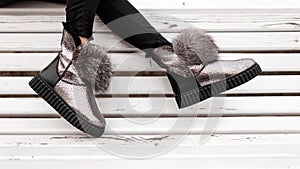 Beautiful silver shiny winter shoes with gray fur on female legs. New collection of fashionable warm glamorous boots. Modern