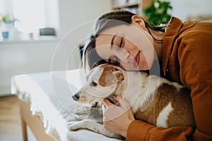 Beautiful single woman lying on bed, snuggling, petting her dog, enjoying weekend. Young woman living alone in apartment