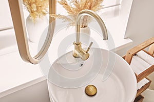 A beautiful sink with a golden faucet next to an oval mirror and a shelf with hand towels. Close-up of an elegant golden