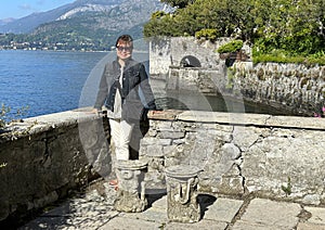 Beautiful sixty-five year-old Korean female tourist posing for a picture in the Garden of Villa Cipressi in Varenna.