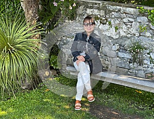 Beautiful sixty-five year-old Korean female tourist sitting on a stone bench in the Garden of Villa Cipressi in Varenna.