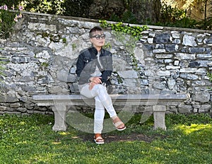 Beautiful sixty-five year-old Korean female tourist sitting on a stone bench in the Garden of Villa Cipressi in Varenna.