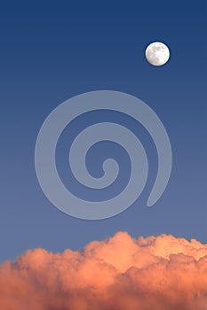 Beautiful sky landscape with white full moon high on clear blue gradient sky above red clouds on sunset