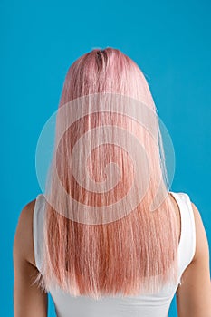 Beautiful sleek natural long pink color dyed hair of young woman standing isolated over blue studio background