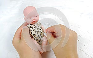 Beautiful sleeping newborn baby doll in the palms of a child, white raised background