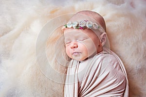 Beautiful sleeping newborn girl with a bandage of flowers on her head