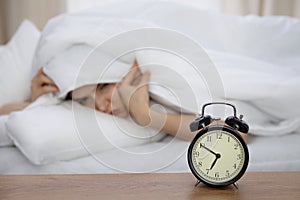 Beautiful sleeping woman lying in bed and trying to wake up with alarm clock. Girl having trouble with getting up early