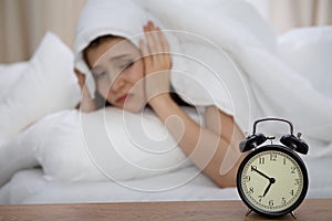 Beautiful sleeping woman lying in bed and trying to wake up with alarm clock. Girl having trouble with getting up early