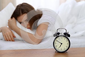 Beautiful sleeping woman lying in bed and trying to wake up with alarm clock. Girl having trouble with getting up early