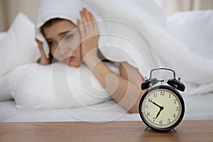 Beautiful sleeping woman lying in bed and trying to wake up with alarm clock. Girl having trouble with getting up early