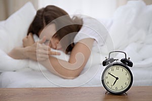 Beautiful sleeping woman lying in bed and trying to wake up with alarm clock. Girl having trouble with getting up early