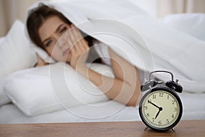 Beautiful sleeping woman lying in bed and trying to wake up with alarm clock. Girl having trouble with getting up early