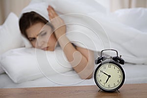 Beautiful sleeping woman lying in bed and trying to wake up with alarm clock. Girl having trouble with getting up early