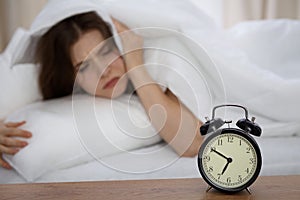 Beautiful sleeping woman lying in bed and trying to wake up with alarm clock. Girl having trouble with getting up early