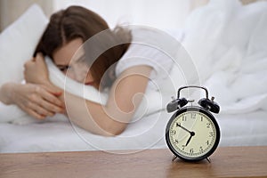 Beautiful sleeping woman lying in bed and trying to wake up with alarm clock. Girl having trouble with getting up early