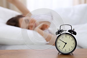 Beautiful sleeping woman resting in bed and trying to wake up with alarm clock