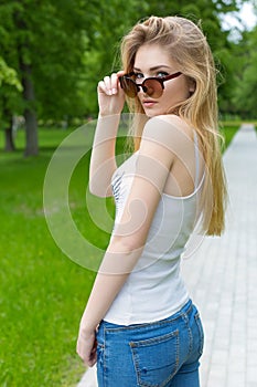 Beautiful slender athletic young girl in sunglasses in jeans and sneakers gleet in the Park summer day