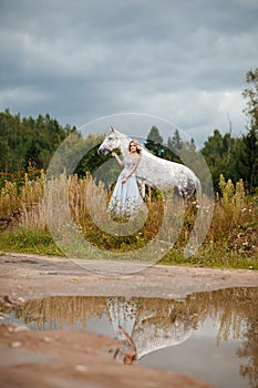 Beautiful slender blonde girl in dress hugging a gray horse, out