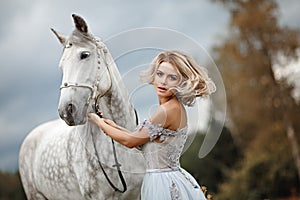 Beautiful slender blonde girl in dress hugging a gray horse, out