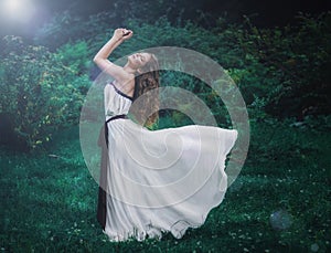 beautiful slender brown-haired young girl with long curly volosvmi in long white dress standing in the middle of a forest