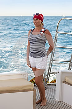 Beautiful slender fellow traveler, pretty woman stands at the stern of a sea yacht against the turquoise sea