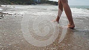 Beautiful slender female legs go along the sandy shore with pebbles along the coast of the sea. sexy female feet walk