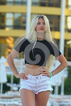 A beautiful slender fitness athletic blonde girl in white shorts and a black short T-shirt, standing by the pool at the hotel in