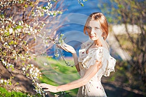 Beautiful slender girl with fair-haired hair in a long light dress against the backdrop of nature, flowering trees, blue sea, ocea