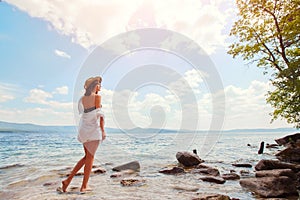 Beautiful slender girl relaxing on the rocky beach of a large lake.