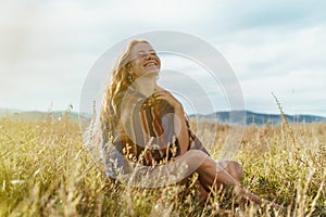 Beautiful slender strong legs peek out from under striped cape on the shoulders of a girl sitting on the grass. throwing