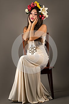 Beautiful slender woman sits in dress on chair with flowers on head