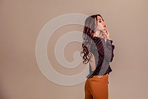 Beautiful slender young girl with black long hair on a one-ton beige background. woman in brown trousers and black blouse with