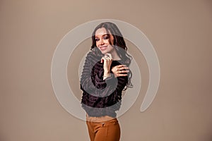 Beautiful slender young girl with black long hair on a one-ton beige background. woman in brown trousers and black blouse with