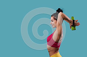 Beautiful and slim athletic woman pumps up the muscles of the biceps and arms with dumbbells while standing sideways on a blue