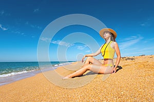 Beautiful slim and attractive caucasian young woman in a yellow swimsuit and top wearing a straw hat enjoys the sea