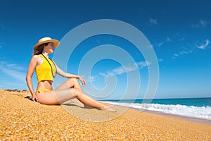 Beautiful slim and attractive caucasian young woman in a yellow swimsuit and top wearing a straw hat enjoys the sea