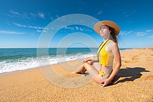 Beautiful slim and attractive caucasian young woman in a yellow swimsuit and top wearing a straw hat enjoys the sea