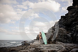 Beautiful slim girl in the multi colored swimsuit sitting near the surf on the rock photo