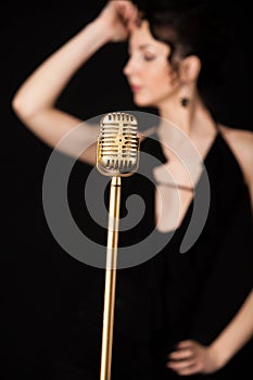 Beautiful slim girl vocalist behind golden vintage microphone