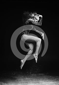 Beautiful slim girl wearing a gymnastic bodysuit covered with clouds of the flying white powder jumps dancing on a dark. Artistic