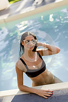 Beautiful slim woman in bikini and sunglasses relaxing and sunbathing on poolside of a swimming pool