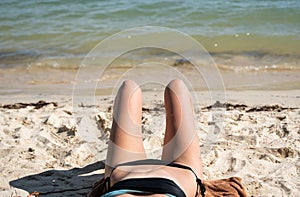 Beautiful slim women`s legs on the beach. Lower half of the girl body lying on the beach by the sea. Young women`s wet