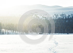 A beautiful small cabin on a shore of lake in central Norway. Snowy winter landscape.